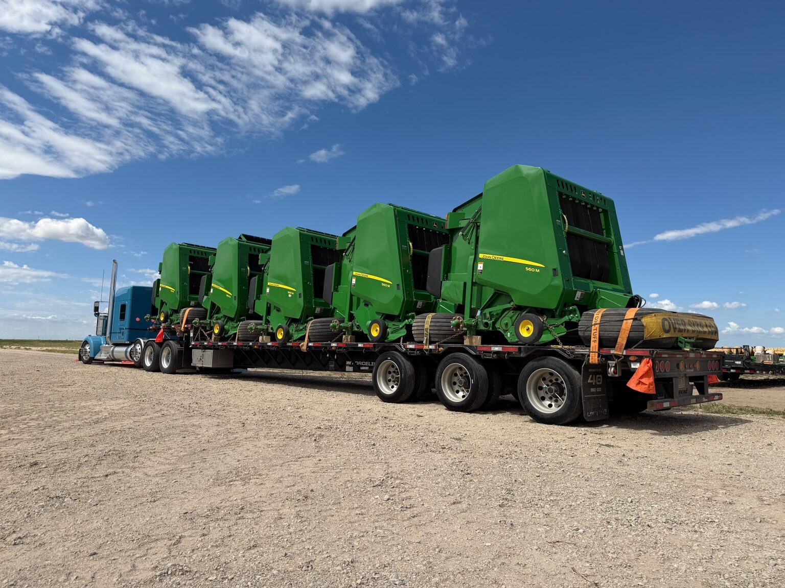 Five John Deere round balers secured on a transport trailer